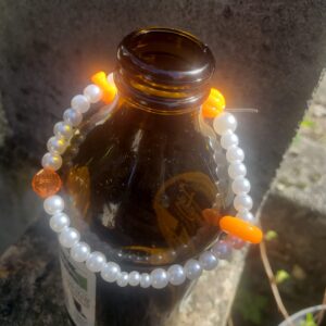 Pearl bracelet with orange beads draped on a brown beer bottle