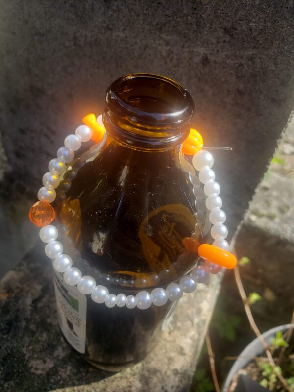 Pearl bracelet with orange beads draped on a brown beer bottle